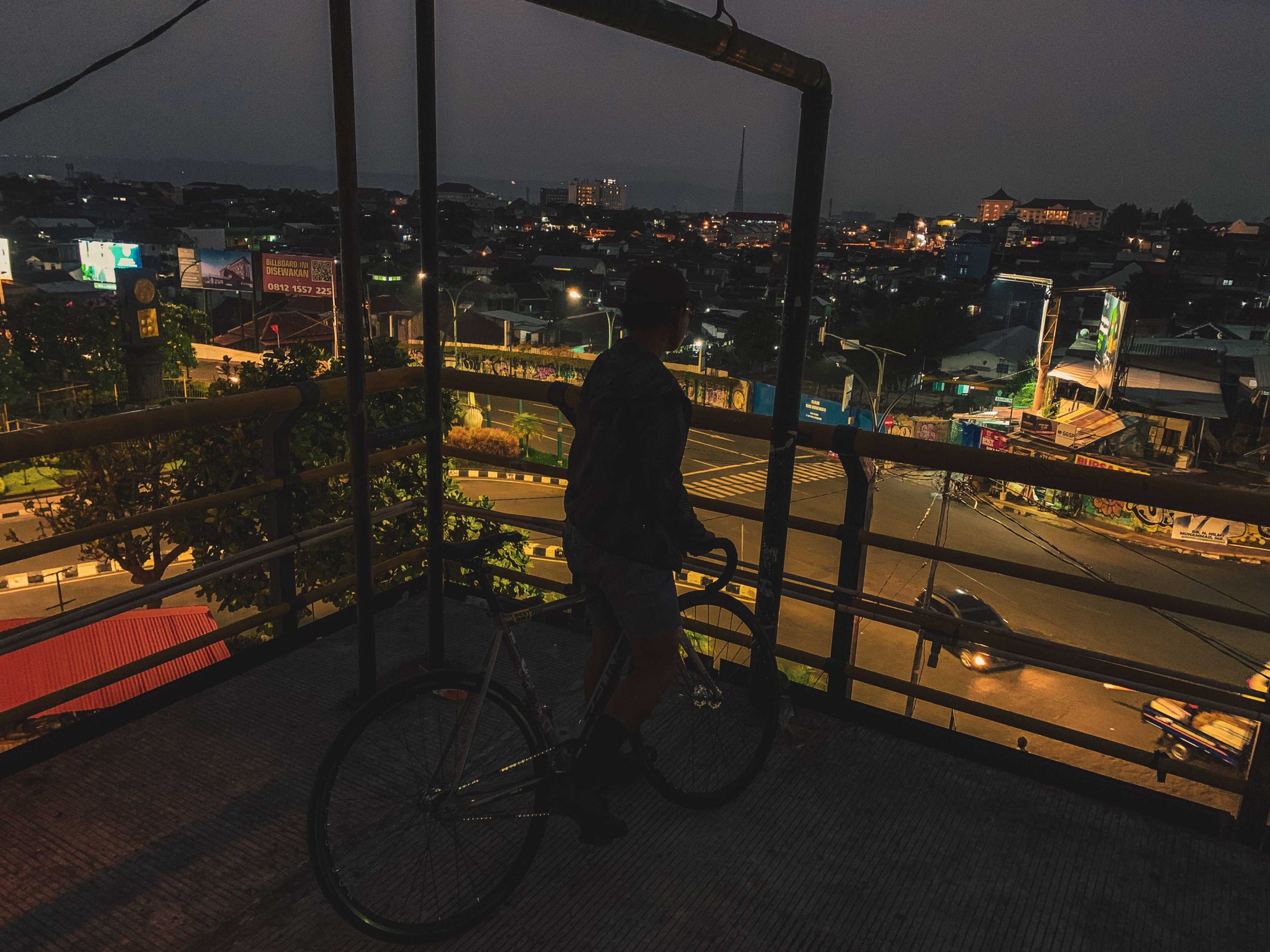 fixed gear cyclist sedang berada di tepi parking lot abu bakar ali melihat keadaan sekitar di tengah kota dengan cahaya city light yang memukau
